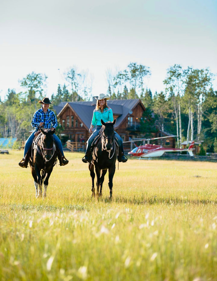 Two horseback riders with the Siwash Lake Wilderness Resort and a helicopter in the background